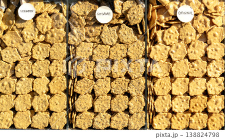 Assorted savory crackers in seaweed, sesame, and original flavors. Neatly organized in clear market containers with circular labels. Golden brown crispy snacks for retail or food industry concepts. Assorted savory crackers in seaweed, sesame, and original flavors. Neatly organized in clear market containers with circular labels. Golden brown crispy snacks for retail or food industry concepts. 138824798