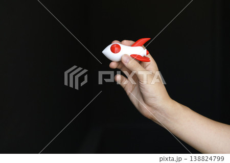 Human hand holding a white and red toy rocket model against a plain black background. Business startup, innovation, and growth mission concept. Minimalist studio shot for success and ambition. Human hand holding a white and red toy rocket model against a plain black background. Business startup, innovation, and growth mission concept. Minimalist studio shot for success and ambition. 138824799