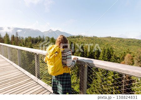 Happy woman with yellow backpack on wooden pedestrian bridge enjoying mountain scenery. Happy woman with yellow backpack on wooden pedestrian bridge enjoying mountain scenery. 138824831