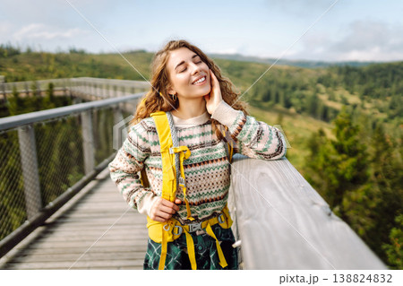 Happy woman with yellow backpack on wooden pedestrian bridge enjoying mountain scenery. Happy woman with yellow backpack on wooden pedestrian bridge enjoying mountain scenery. 138824832