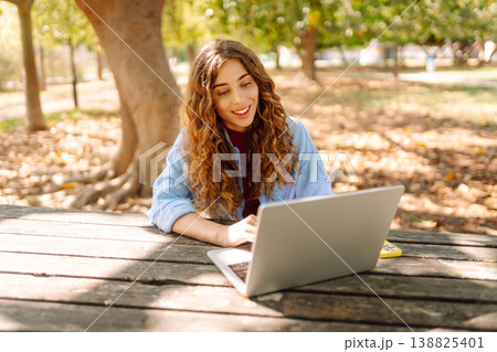 Attractive woman working or studying at laptop as sitting in city park. Freelancer working in park. Attractive woman working or studying at laptop as sitting in city park. Freelancer working in park. 138825401