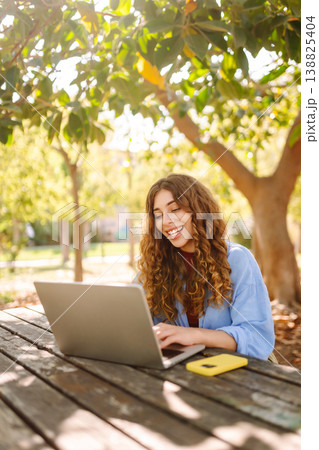 Attractive woman working or studying at laptop as sitting in city park. Freelancer working in park. Attractive woman working or studying at laptop as sitting in city park. Freelancer working in park. 138825404