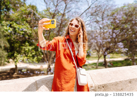 Young woman taking a cheerful selfie in blooming park on a sunny day. Joy concept. Active lifestyle. 138825435