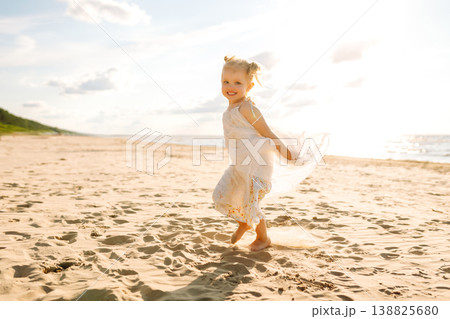 Young girl joyfully plays on the sandy beach during sunset, enjoying a carefree moment by the ocean 138825680