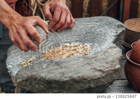 Human hand rotating an ancient stone grinding machine for smashing grains. Handmade manual equipment grind mill 138825687