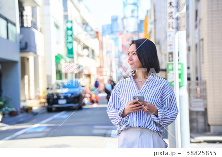 買い出しの途中にスマホを見て微笑む日本人女性。休日の街角での散歩。 138825855