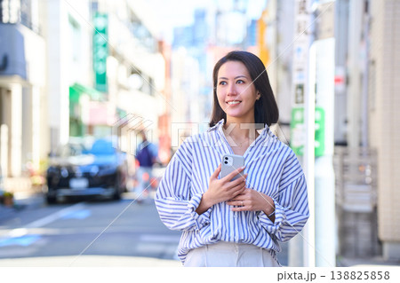 買い出しの途中にスマホを見て微笑む日本人女性。休日の街角での散歩。 138825858