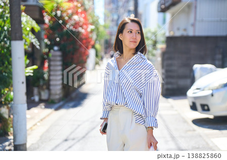 買い出しの途中にスマホを見て微笑む日本人女性。休日の街角での散歩。 138825860