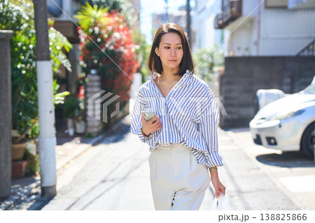 買い出しの途中にスマホを見て微笑む日本人女性。休日の街角での散歩。 138825866
