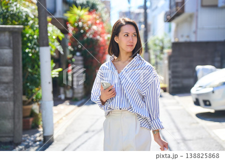 買い出しの途中にスマホを見て微笑む日本人女性。休日の街角での散歩。 買い出しの途中にスマホを見て微笑む日本人女性。休日の街角での散歩。 138825868