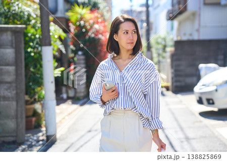 買い出しの途中にスマホを見て微笑む日本人女性。休日の街角での散歩。 買い出しの途中にスマホを見て微笑む日本人女性。休日の街角での散歩。 138825869