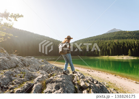 Back view young woman with backpack looking the view of the mountain lake in sunny weather. 138826175