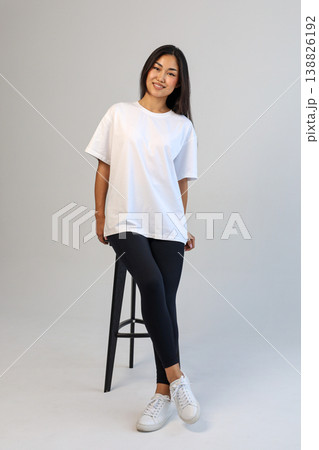Casual Asian content creator dressed in white shirt relaxing on stool for social media visuals 138826192