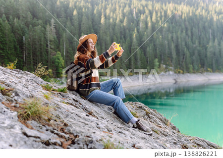 Young woman takes a photos the nice view by the serene lake surrounded by forested mountains Young woman takes a photos the nice view by the serene lake surrounded by forested mountains 138826221
