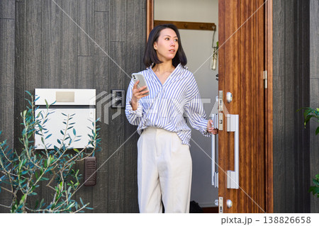 スマホを手に一軒家の玄関から外出する日本人女性 138826658