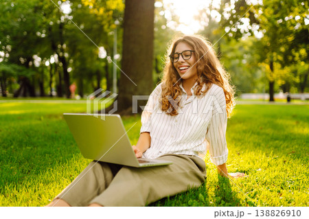 Happy Woman with laptop sit green grass at park. Studying outdoors. Freelancing concept 138826910