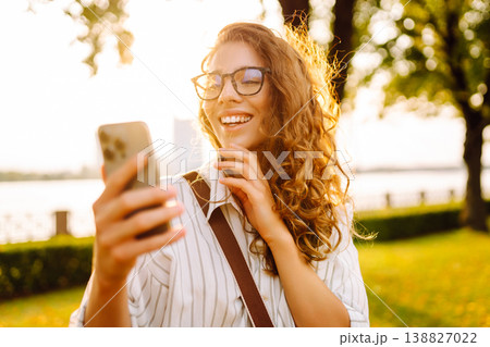 Happy woman enjoying sunset on the embankment with phone in her hands. City life concept. Happy woman enjoying sunset on the embankment with phone in her hands. City life concept. 138827022