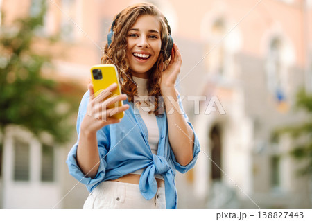Happy relaxed woman in wireless headphones choosing, listening favorite music in urban city street. 138827443