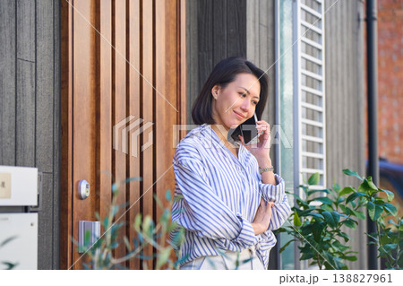 住宅の玄関前で電話をする日本人女性の横顔 138827961
