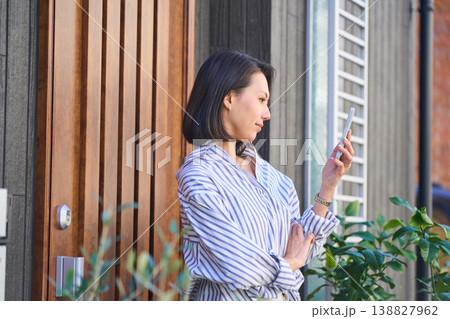 住宅の玄関前でスマホを確認する日本人女性の横顔 138827962