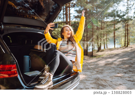Happy Woman is resting in trunk of car and taking selfie. Travel, tourism, nature, active life. Happy Woman is resting in trunk of car and taking selfie. Travel, tourism, nature, active life. 138828003