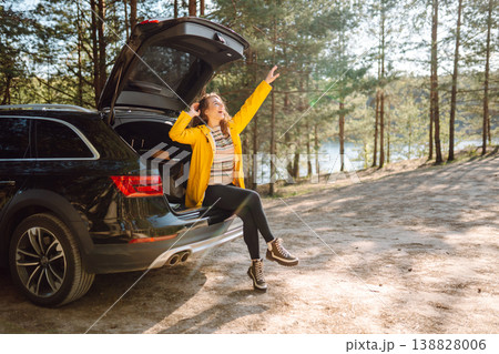 Young woman sits in the trunk of a car in forest. The concept of traveling by car, active lifestyle. 138828006