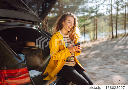 Young woman sitting in open trunk with phone. Lifestyle, travel, tourism, nature, active life. 138828007