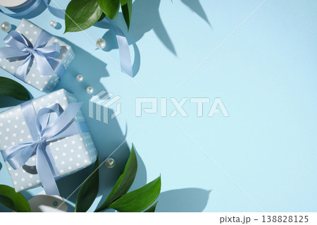 Blue polka dot gift boxes with satin ribbons, green leaves, and pearls on a light blue background. Copyspace Blue polka dot gift boxes with satin ribbons, green leaves, and pearls on a light blue background. Copyspace 138828125