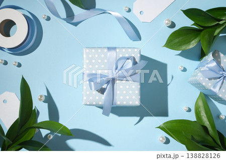 Elegant blue gift box with ribbon bow, pearls and green leaves on pastel background. 138828126