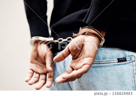 Back, arrest and handcuffs with a man suspect of a crime by law enforcement closeup on a gray background. Security, jail or prison with a male criminal handcuffed from behind for legal justice 138828983