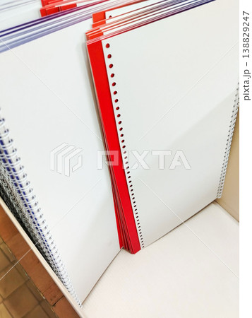 Stack of spiral-bound notebooks with blank white pages and a red cover, arranged neatly on a shelf in a stationery store Stack of spiral-bound notebooks with blank white pages and a red cover, arranged neatly on a shelf in a stationery store 138829247