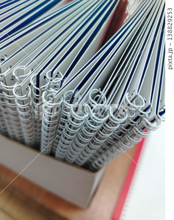 Stack of spiral-bound notebooks with white pages and blue covers arranged neatly in a box on a wooden surface, showcasing the binding and page edges Stack of spiral-bound notebooks with white pages and blue covers arranged neatly in a box on a wooden surface, showcasing the binding and page edges 138829253