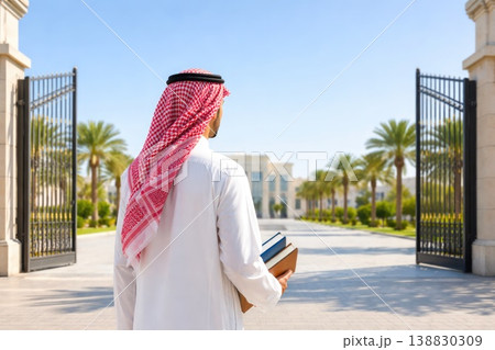 Arab male student walking toward university campus holding books in sunny day Arab male student walking toward university campus holding books in sunny day 138830309