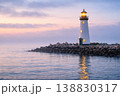 Lighthouse on rocky shore at sunset with glowing light over calm sea 138830317