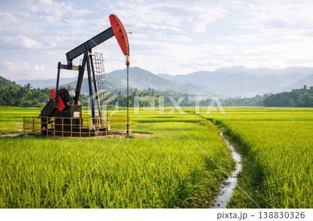 Oil drilling pumpjack in lush rice field landscape with mountains and blue sky 138830326
