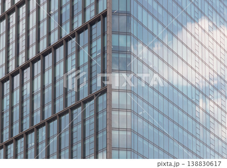 Sharp angles and rhythmic grids define this modern facade. The building bronze frame creates a sense of rigid order, beautifully disrupted by the soft, atmospheric clouds reflected across its sleek 138830617