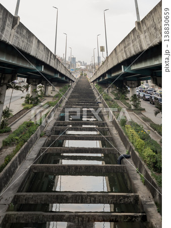 Framed by twin concrete overpasses, a weathered utility span recedes in sharp perspective toward a distant city skyline. A rhythmic ladder of parallel beams arches over a reflective channel, while Framed by twin concrete overpasses, a weathered utility span recedes in sharp perspective toward a distant city skyline. A rhythmic ladder of parallel beams arches over a reflective channel, while 138830659