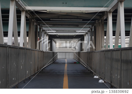 Framed by a symmetrical array of weathered white trusses, this industrial pedestrian overpass stretches forward in a clean, linear perspective. Framed by a symmetrical array of weathered white trusses, this industrial pedestrian overpass stretches forward in a clean, linear perspective. 138830692