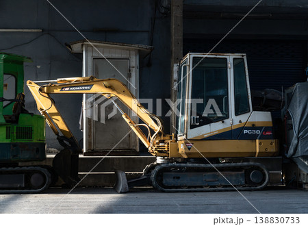 The machine vibrant yellow arm, etched with the patina of hard labor, creates a bold diagonal slash across the frame, its hydraulic cylinders gleaming where the sunlight catches the metal. The cab, a 138830733