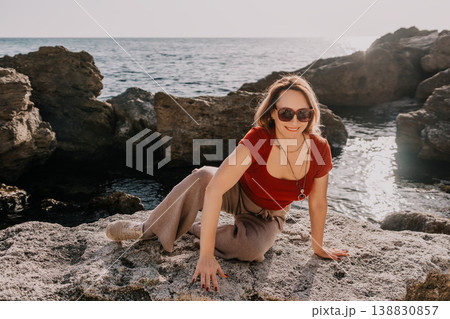 Woman coast rocks smiling woman sitting on a rugged rocky shoreline by the sea during a sunny vacation Woman coast rocks smiling woman sitting on a rugged rocky shoreline by the sea during a sunny vacation 138830857