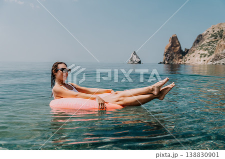 Swimming vacation ocean woman relaxes on a pink inflatable ring in crystal clear sea water near coastal cliffs 138830901