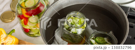 People prepare jars of cucumbers and peppers for canning in the kitchen. The process involves boiling jars to seal them for winter use. Fresh ingredients are used, banner People prepare jars of cucumbers and peppers for canning in the kitchen. The process involves boiling jars to seal them for winter use. Fresh ingredients are used, banner 138832796