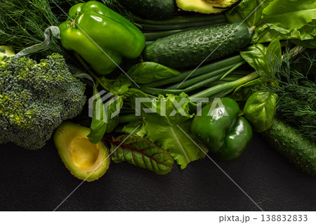 A variety of fresh green vegetables is neatly arranged on a dark surface, showcasing cucumbers, bell pepper, avocado, broccoli, and various leafy greens, healthy eating for a nutritious salad 138832833
