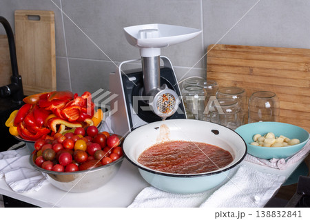 Fresh vegetables are being ground to prepare Adjika in a kitchen. Bright carrots, tomatoes, and peppers are added to a large bowl for a spicy Georgian seasoning Fresh vegetables are being ground to prepare Adjika in a kitchen. Bright carrots, tomatoes, and peppers are added to a large bowl for a spicy Georgian seasoning 138832841