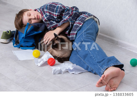 Young boy lies on the floor resting with a cat surrounded by colorful toys and crumpled paper in a cozy indoor setting Young boy lies on the floor resting with a cat surrounded by colorful toys and crumpled paper in a cozy indoor setting 138833605