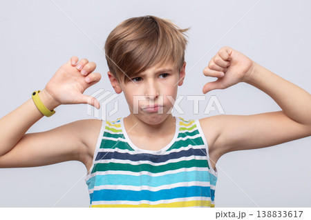 Young boy expresses disappointment with thumbs down gesture against a light background Young boy expresses disappointment with thumbs down gesture against a light background 138833617