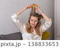 Woman styling her hair at home with a yellow hair accessory while wearing a satin top 138833653