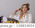 Woman styling her long hair while seated at a vanity in a cozy indoor setting during daylight hours 138833654