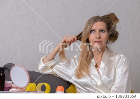 Woman styling her long hair while seated at a vanity in a cozy indoor setting during daylight hours 138833654