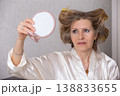 Woman checking hairstyle in mirror while wearing a silk robe at home during morning routine 138833655